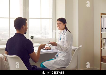 Positive Frau medizinische Arbeiter sitzen und geben Papier verschreiben zu Mann, Patient Stockfoto