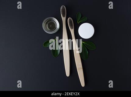 Zwei Holz Bambus umweltfreundliche Zahnbürsten, Gebiss und grüne Blätter auf schwarzem Hintergrund. Stockfoto