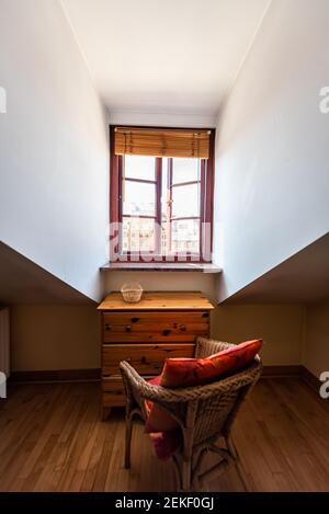 Schräge Kathedrale Decke und Fenster in Loft vertikale Ansicht mit Tisch und Stuhl im dunklen Schlafzimmer Haus Apartment Zimmer in Europa Stockfoto