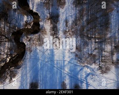 Flug über den Winterpark. Die Drohne schlopt über den Fluss, Kamera nach unten. Luftaufnahmen der Winterlandschaft. Stockfoto