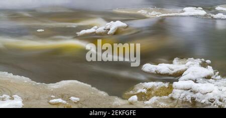 Winter fließendes Wasser mit Details von schmelzendem Schnee und Eis in abstraktem Hintergrund. Nahaufnahme der dynamischen Flussoberfläche mit wunderschönen Bewegungsunschärfen. Stockfoto