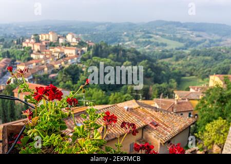 Chiusi, Italien Dachziegel Ansicht mit historischen alten mittelalterlichen Gebäuden der Stadt Dorf im Sommer mit Vordergrundrahmen von roten Geranienblumen Stockfoto