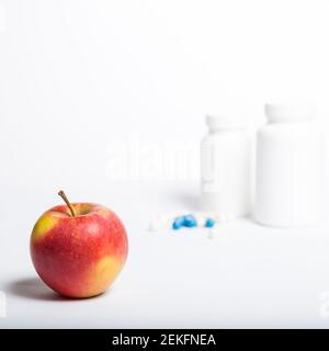 Roter Apfel verschließend und blaue und weiße Pillen von conteiners auf weißem Hintergrund. Stockfoto