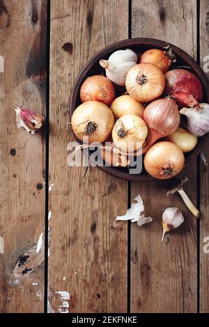 Gelbe, rote Zwiebeln und Knoblauch in einer Schüssel auf Holzgrund. Stockfoto