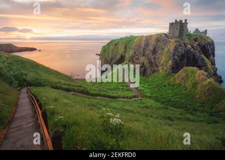 Goldenes Sonnenaufgang oder Sonnenuntergang Licht auf der Küstenlandschaft Ruinen von Donnottar Castle an der Aberdeenshire Küste von Schottland. Stockfoto