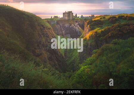 Goldenes Sonnenaufgang oder Sonnenuntergang Licht auf der Küstenlandschaft Ruinen von Donnottar Castle an der Aberdeenshire Küste von Schottland. Stockfoto