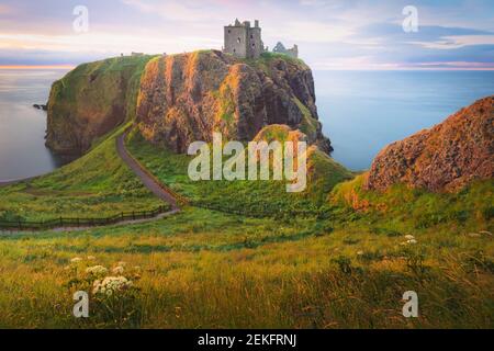 Goldenes Sonnenaufgang oder Sonnenuntergang Licht auf der Küstenlandschaft Ruinen von Donnottar Castle an der Aberdeenshire Küste von Schottland. Stockfoto