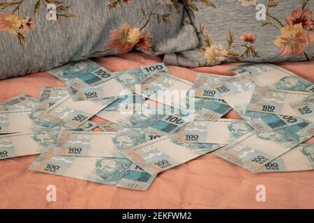 Brasilianisches Geld verstreut auf dem Bett, hundert reais, ein romantisches Schlafzimmer. Das Konzept des Nachtlebens, oder die Kosten für die Einrichtung einer Wohnung Stockfoto