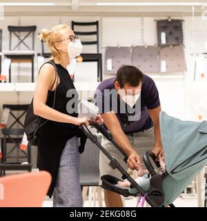 Junges Paar mit Neugeborenen im Kinderwagen Einkaufen im Einzelhandel Möbel Und Wohnaccessoires speichern Tragen schützende medizinische Gesichtsmaske zu Verhindern Stockfoto
