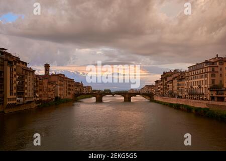 Blick auf die Brücke der Heiligen Dreifaltigkeit und den Fluss Arno von Ponte Vecchio, umgeben von malerischen Gebäuden unter einem wunderschönen Sonnenuntergang Himmel an einem Frühlingstag i Stockfoto