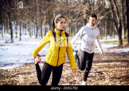 Portrait-Ansicht der fokussierten gut aussehend fleißige sportliche Fitness-Mädchen im Winter Sportswear Stretching außerhalb mit Personal Trainer in der Natur. Stockfoto