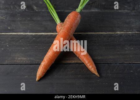 Zwei gekreuzte frische Karotten auf Holzhintergrund.Draufsicht auf Creative Gesunde Ernährung Mockup Konzept Stockfoto