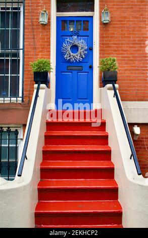 Blaue Eingangstür auf Backstein in Brooklyn, New York, NYC, USA. Rot gestrichene Stufen führen bis zur Eingangstür an dieser Fassade des Wohngebäudes. Stockfoto