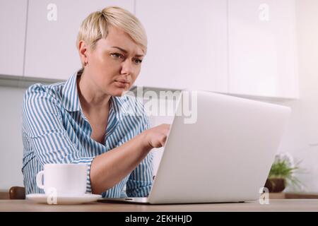 Fokussierte ernsthafte Frau arbeiten auf Laptop zu Hause Frau mit Tragbarer Computer in der Küche Stockfoto