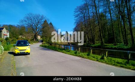 Ein gelbes Auto in der Nähe eines Dorfbaches (thornton Beck) bei Thornton le Dale (aka Thornton Dale), in der Nähe von Pickering, North, Yorkshire. Thornton-le-Dale (früher Torentune genannt) gilt oft als einer der schönsten in Yorkshire. Es war früher eine Handwebmaschine Weben Township und liegt in der Nähe Dalby Wald. Und die alte sächsische / normannische Kirche St. Hilda Ellerburn. Stockfoto