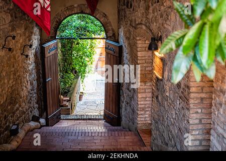 Montalcino, Italien - 26. August 2018: Historisches Dorf in der Toskana Sommer mit roten Fahnen Banner in Hotel Rezeption Durchgang zum Garten auf der Straße Stockfoto