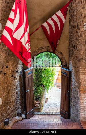 Montalcino, Italien - 26. August 2018: Kleines historisches Dorf in der Toskana Sommer mit roten Fahnen Banner in Durchgang zum Garten auf Straße Stein Stadt Stockfoto