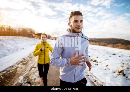 Nahaufnahme Porträt von glücklich lächelnd fokussierten gut aussehend fleißend Aktiver Fitness-Mann im Winter Sportbekleidung mit Ohrhörer laufen mit Ein wunderschönes s Stockfoto