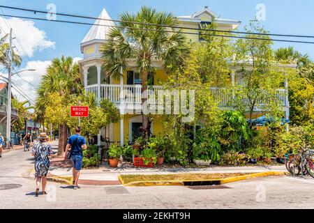 Key West, USA - 1. Mai 2018: Wohnstraße mit Menschen, die im Sommer an einem bunten gelben Strandhaus auf Florida Keys Island vorbei fahren Stockfoto