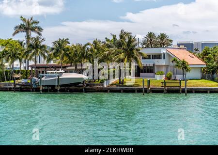 Bal Harbour, USA - 8. Mai 2018: Wohlhabendes, reiches Einfamilienhaus mit Dock und Boot, das am Wasser in Miami Florida mit hellgrünem Turquo angedockt ist Stockfoto