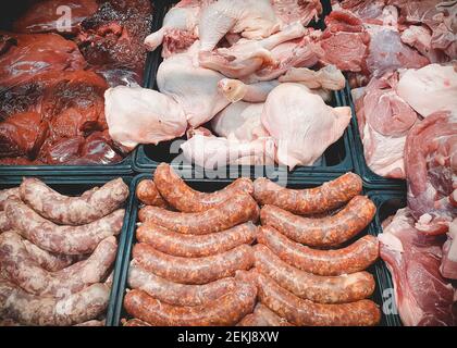Verschiedene frische rohe Fleisch- und Fleischprodukte auf der Markttheke. Würstchen, Hühnerteile und Leber Stockfoto