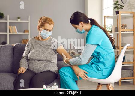 Ältere Frau sitzt auf dem Sofa zu Hause und bekommen Grippe Impfstoffinjektion in ihrem Arm Stockfoto