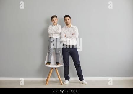 Lächelnder Vater und Sohn in stilvoller Freizeitkleidung und Sneakers Stehen mit gekreuzten Händen Stockfoto