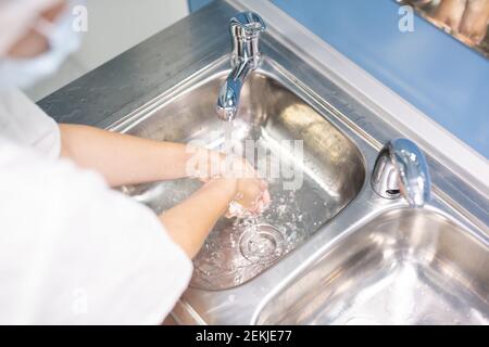 Junge Assistentin, Krankenschwester oder Arzt in weißer Uniform waschen Hände über einem von zwei metallischen Waschbecken vor oder nach dem medizinischen Eingriff in Kliniken Stockfoto