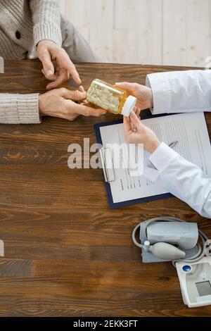Überblick über die Hände des Hausarztes vorbei Flasche Pillen Zu kranken älteren männlichen Patienten über Tisch mit medizinischen Papier Und Tonometer Stockfoto