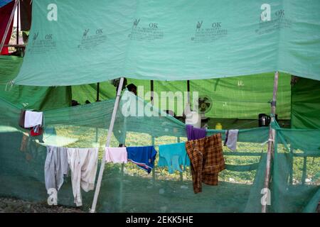 YANGON, MYANMAR - DECEMEBER 31 2019: Ein burmesischer Mann sitzt unter einer grünen Plane neben einem Ventilator in der Hitze, während die Wäsche draußen trocknet Stockfoto