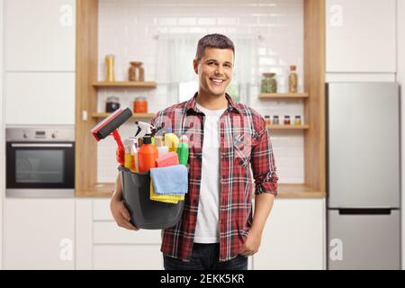 Junger Mann lächelt und hält einen Eimer voller Reinigung Lieferungen in einer Küche Stockfoto