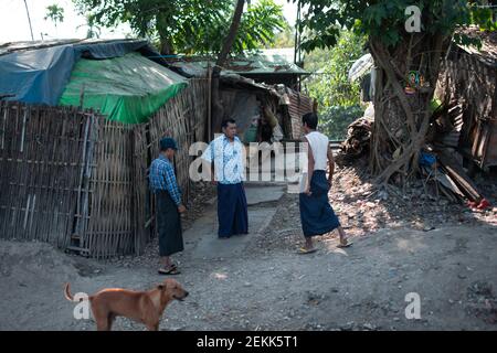 YANGON, MYANMAR - DECEMEBER 31 2019: Drei burmesische Männer im traditionellen Longyi, die ein Gespräch führen, während der Kreiszug vorbeifährt Stockfoto