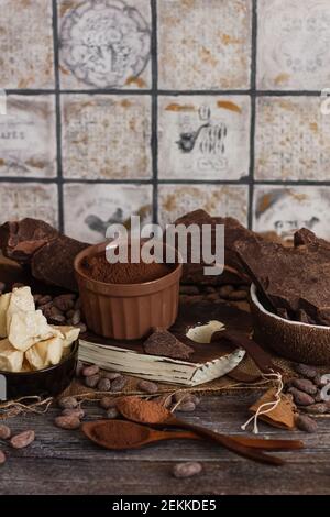 Ungesüßte Backblockschokolade, Kakaopulver, Kakaobutter und Kakaobohnen auf altem Holzhintergrund Stockfoto