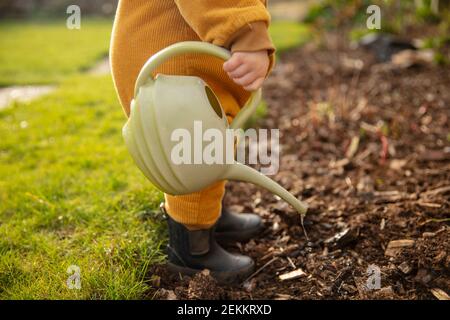 Ein kleines Kind hilft im Garten Pflanzen wässern Mit einer Gießkanne Stockfoto