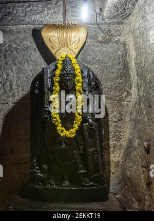 Chitradurga, Karnataka, Indien - 10. November 2013: Fort oder Elusuttina Kote. Schwarze Shiva-Statue mit gelber lei im Inneren Sanctum mit Shivalingam und N Stockfoto