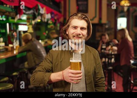 Porträt eines jungen Mannes, der die Kamera anschaut und Bier trinkt In der Bar Stockfoto