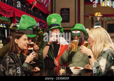 Gruppe von Freunden in grünen Hüten sitzen am Tisch Bier trinken und Patricks Day in der Bar feiern Stockfoto