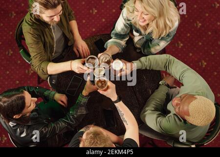 Blick aus der Perspektive auf eine Gruppe von Freunden, die an der sitzen Tischtoasten mit Bier während ihres Treffens in der Bar Stockfoto