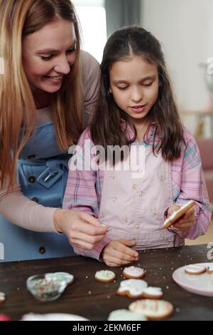 Junge glückliche Mutter mit Tochter Kochen und Dekoration Cookies an Der Tisch und die Vorbereitung für Ostern Stockfoto