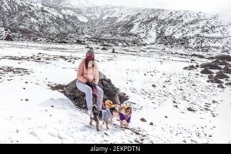 Teen Mädchen mit Maske sitzt mit ihren Hunden auf einem Schneebedeckter Berg Stockfoto