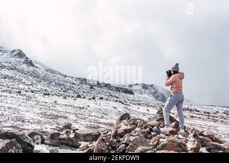 Fotografin auf Felsen stehend und Landschaftsfotos auf Ein schneebedeckter Berg inmitten von Wolken und Nebel Stockfoto