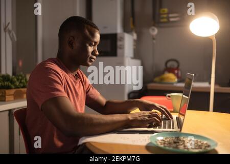 Schwarzer Mann, der auf der Laptop-Tastatur beim Arbeiten auf der Fernbedienung tippt Projekt zu Hause Stockfoto