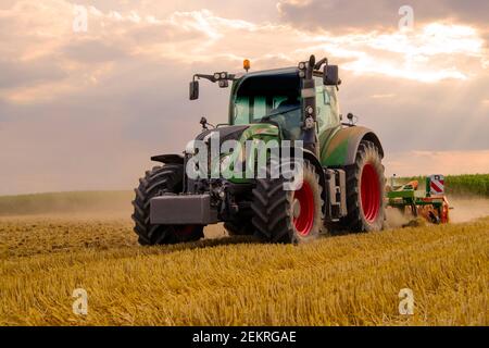 Grüner Traktor pflügt Getreidefeld mit Himmel mit Wolken Stockfoto