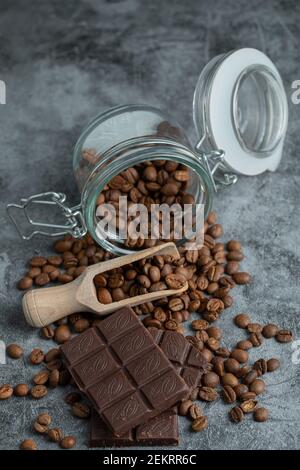 Ein Glas voller Kaffeebohnen mit Schokoriegel Auf grauem Hintergrund Stockfoto