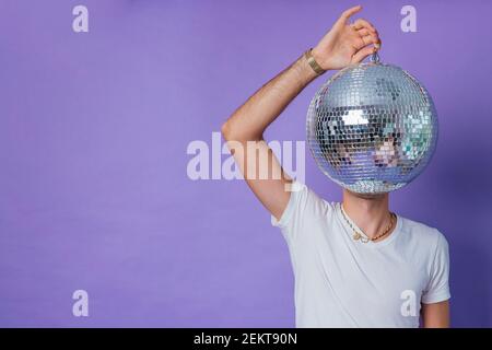 Mann in einem weißen T-Shirt mit einem Spiegelball als Kopf auf einem lila Hintergrund. Speicherplatz kopieren. Stockfoto