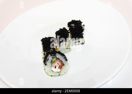 Sushi-Rollen california mit schwarzem Kaviar liegen auf weißem Teller. Japanische Küche, europäische Sushi-Brötchen mit Frischkäse, Lachs, Garnelen und Avocado Stockfoto