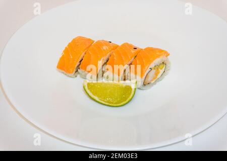 Sushi-Brötchen philadelphia mit Garnelen und Limettenscheibe liegen auf weißem Teller. Japanische Küche, europäische Sushi-Brötchen mit Frischkäse, Lachs und Garnelen Stockfoto