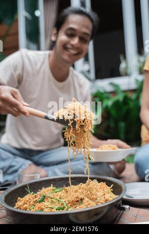Nahaufnahme des jungen Mannes, der einen Löffel voll nimmt Noodle während Picknick mit Freund Stockfoto