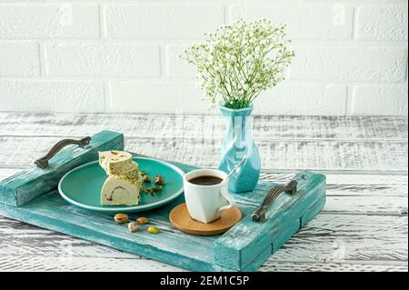 Frühstück am Morgen - Pistaschio Halva in Scheiben geschnitten mit Tasse Kaffee auf einem blauen Holztablett mit Blumen. Stockfoto