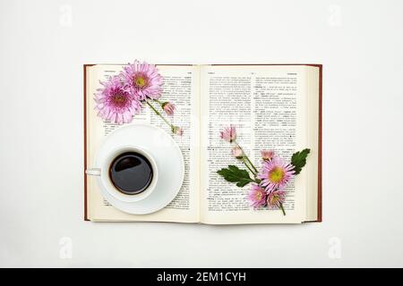 Lesen eines Buches im Frühjahr. Ein Buch mit frischen Frühlingsblumen und einer Tasse Kaffee. Gemütlicher Morgen mit erfrischendem schwarzen Kaffee und einem interessanten Buch Stockfoto